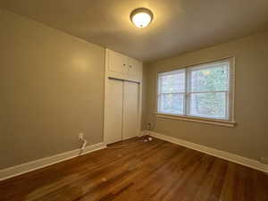 Unfurnished bedroom featuring a closet, baseboards, and dark wood-type flooring