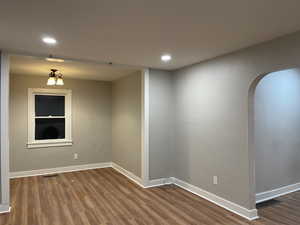 Unfurnished room with baseboards, visible vents, arched walkways, and wood finished floors