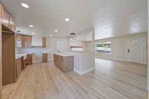 Kitchen with brown cabinetry, light wood-style floors, recessed lighting, tasteful backsplash, and decorative light fixtures