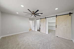 Unfurnished bedroom featuring baseboards, a barn door, and carpet