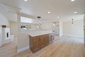 Kitchen with brown cabinetry, a textured ceiling, baseboards, and light wood-type flooring
