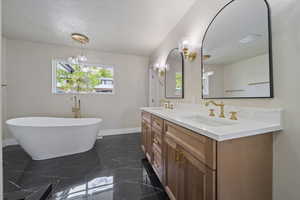 Bathroom featuring double vanity, a textured ceiling, a freestanding bath, a sink, and baseboards