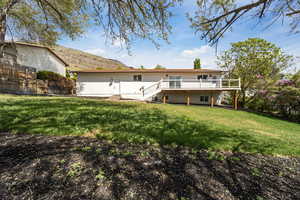 Rear view of house featuring fence, stairs, a wooden deck, and a lawn