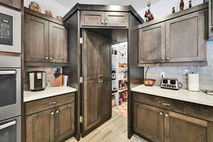 Kitchen with light wood-style flooring, dark brown cabinets, tasteful backsplash, and black microwave