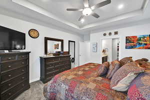 Bedroom featuring a raised ceiling, ensuite bathroom, dark carpet, recessed lighting, and baseboards