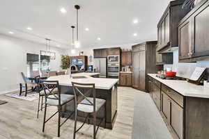 Kitchen featuring a center island with sink, a sink, stainless steel appliances, light countertops, and decorative backsplash