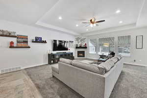 Living room with baseboards, visible vents, ceiling fan, a tiled fireplace, and a raised ceiling