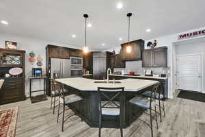 Kitchen featuring backsplash, light countertops, appliances with stainless steel finishes, a kitchen breakfast bar, and a sink