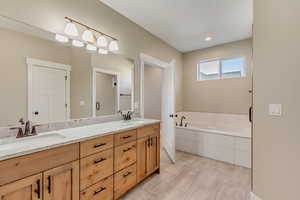 Main floor primary bathroom featuring a garden tub, double vanity, a dual head shower with shower door, and dual sinks.