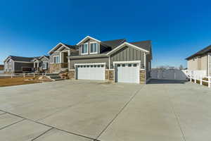 Craftsman-style house featuring stone siding, board and batten siding, driveway, and fence