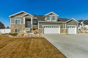 Craftsman inspired home featuring board and batten siding, a front lawn, fence, a garage, and stone siding