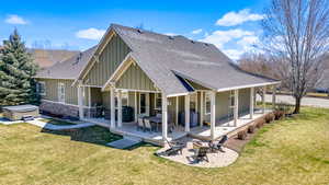 Back of house with roof with shingles, a fire pit, board and batten siding, a hot tub, and a lawn