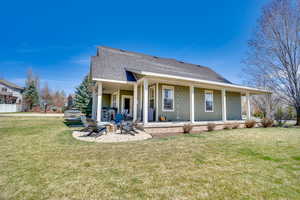 Rear view of house with an outdoor fire pit, a shingled roof, a patio area, and a lawn