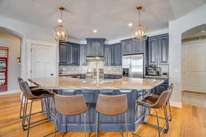 Kitchen with under cabinet range hood, arched walkways, light wood-style floors, stainless steel fridge with ice dispenser, and decorative backsplash