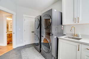 Washroom featuring tile patterned floors, a sink, stacked washing maching and dryer, cabinet space, and baseboards