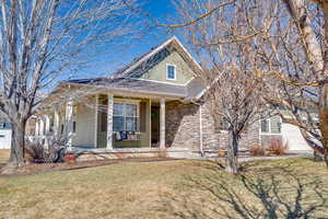 View of front of home featuring a shingled roof, a front lawn, a porch, stone siding, and an attached garage