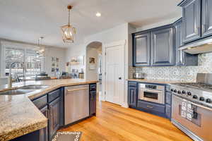 Kitchen featuring tasteful backsplash, under cabinet range hood, light wood-style flooring, stainless steel appliances, and a sink