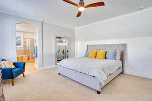 Bedroom with arched walkways, light carpet, baseboards, and ornamental molding