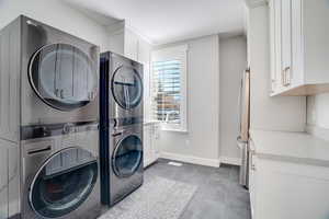 Clothes washing area featuring stacked washer / dryer, cabinet space, and baseboards