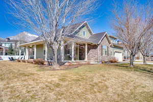 View of front of property featuring stone siding, covered porch, a front lawn, and a garage