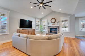 Living room with a stone fireplace, vaulted ceiling, baseboards, and light wood-type flooring