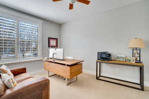 Home office featuring light colored carpet, baseboards, and ceiling fan