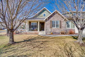 View of front of house with a porch, stone siding, board and batten siding, and a front lawn