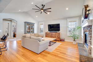 Living area featuring arched walkways, light wood-style floors, a stone fireplace, and vaulted ceiling