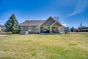 Back of property with board and batten siding, a hot tub, a yard, a patio area, and a shingled roof