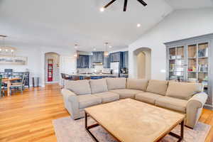 Living area with baseboards, light wood-type flooring, recessed lighting, arched walkways, and high vaulted ceiling