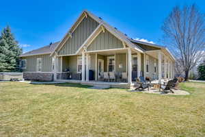 Back of property featuring a fire pit, a hot tub, a patio area, a yard, and board and batten siding