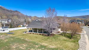 Back of house with a mountain view, roof with shingles, fence, and a lawn