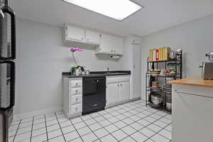 Kitchen featuring dishwasher, white cabinets, baseboards, and a sink