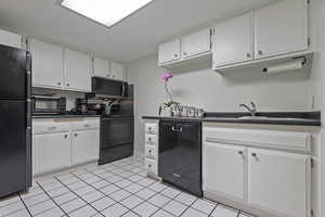 Kitchen with black appliances, white cabinets, dark countertops, and a sink