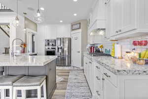 Kitchen featuring a kitchen bar, appliances with stainless steel finishes, custom exhaust hood, white cabinetry, and a sink