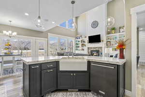 Kitchen featuring light wood finished floors, open floor plan, dishwasher, a stone fireplace, and a sink