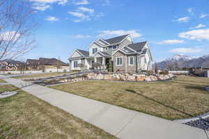 View of front of home featuring stone siding, a mountain view, a front yard, and fence