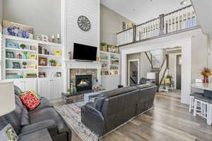 Living area featuring a high ceiling, a stone fireplace, wood finished floors, and stairs