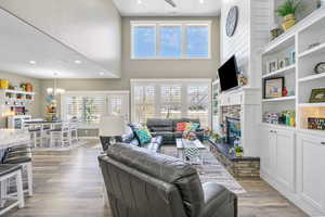 Living room featuring light wood-style flooring, recessed lighting, an inviting chandelier, a fireplace, and a towering ceiling