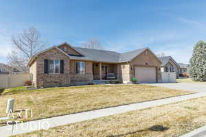 Ranch-style home with fence, driveway, an attached garage, a front lawn, and brick siding