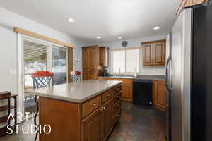 Kitchen featuring a sink, black dishwasher, stone tile floors, freestanding refrigerator, and brown cabinetry