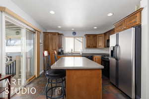 Kitchen featuring a center island, brown cabinetry, stone tile flooring, black appliances, and a sink