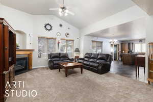 Carpeted living area featuring ceiling fan with notable chandelier, a tile fireplace, high vaulted ceiling, and baseboards