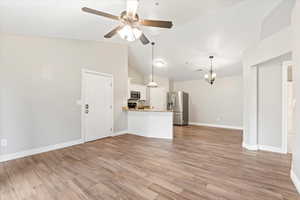 Unfurnished living room with light wood-style flooring, ceiling fan with notable chandelier, baseboards, and vaulted ceiling