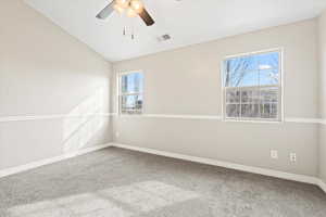 Spare room with visible vents, a ceiling fan, carpet flooring, baseboards, and vaulted ceiling