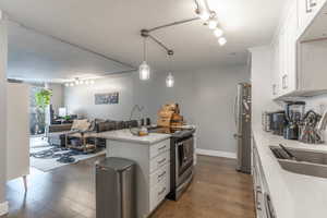 Kitchen with dark wood finished floors, open floor plan, appliances with stainless steel finishes, white cabinets, and a sink