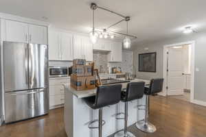 Kitchen with stainless steel appliances, dark wood-type flooring, tasteful backsplash, and white cabinets