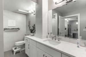 Bathroom featuring tile patterned flooring, toilet, tile walls, and vanity