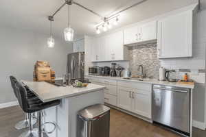 Kitchen with a sink, decorative backsplash, dark wood-type flooring, white cabinets, and appliances with stainless steel finishes