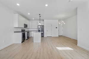 Kitchen featuring a kitchen island with sink, electric stove, open floor plan, light wood finished floors, and light countertops